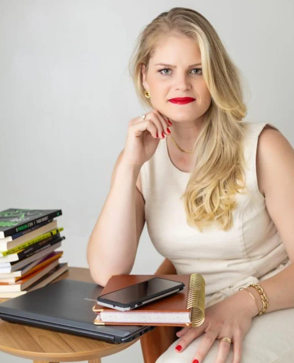 Gláucia Fekete sentada à mesa de trabalho com livros, notebook e planner